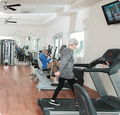 Senior woman on treadmill and another senior on seated exercise machine in the Fitness Center at Fellowship Square Phoenix Independent Living community